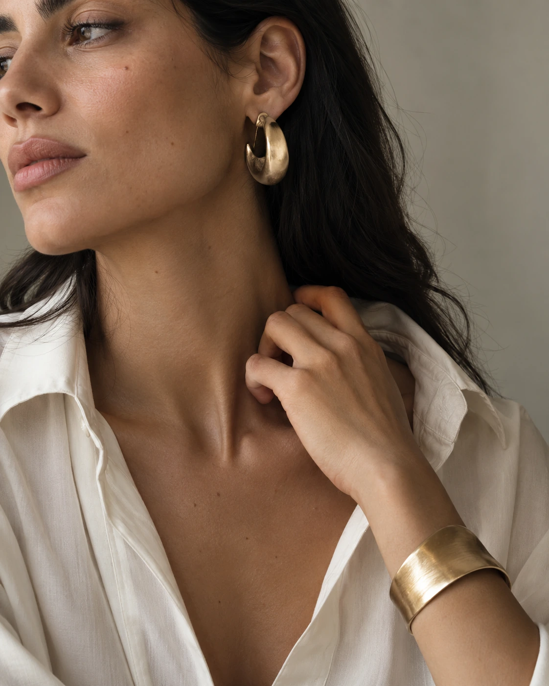 Editorial concept of sculptural gold jewelry worn with an ivory shirt