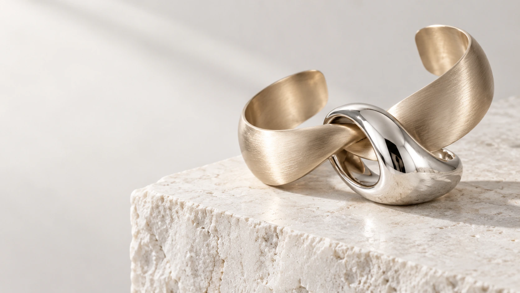 Sculptural champagne gold cuff and silver ring on pale limestone — concept jewelry study